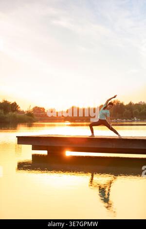 Chinesische Frau mittleren Alters, die Yoga am Pier bei Sonnenuntergang macht Stockfoto