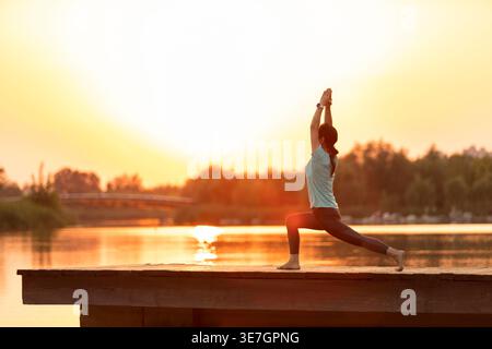 Chinesische Frau mittleren Alters, die Yoga am Pier bei Sonnenuntergang macht Stockfoto
