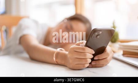 Asiatische Frau schläft ein, während sie ihr Smartphone zu Hause auf den Tisch legt Stockfoto