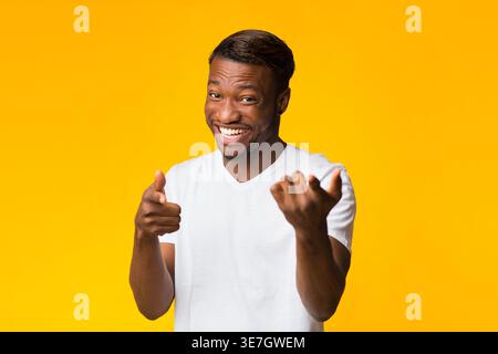 Schwarzer Mann in weißem Hemd, der Finger auf gelbem Hintergrund im Studio zeigt Stockfoto