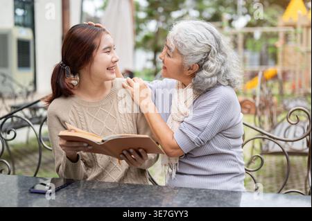Thai Senior Frau, die Spaß beim Lesen von Büchern mit ihrer Enkelin hat, während sie tagsüber am Tisch im Garten sitzt Stockfoto
