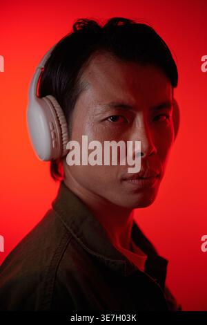 Asiatischer Mann mit Kopfhörern, die seitlich vor rotem Neonhintergrund stehen Stockfoto