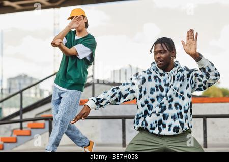Schwarze und asiatische Männer in Street Style Kleidung tanzen auf der Fußgängerbrücke in der Stadt Stockfoto
