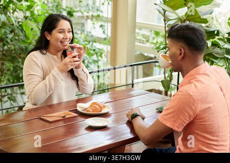 Asiatische Freundinnen und Freunde unterhalten sich mit Saft und Kaffee, während sie am Tisch im Café sitzen Stockfoto