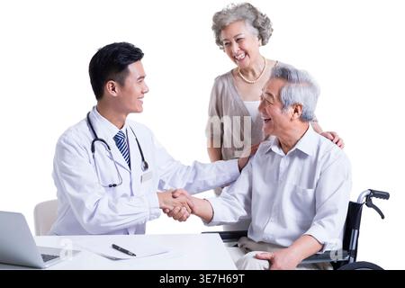 Ein lächelnder chinesischer Arzt schüttelt einem älteren chinesischen Mann die Hand, während er in der Nähe einer älteren chinesischen Frau vor weißem Hintergrund im Studio sitzt Stockfoto