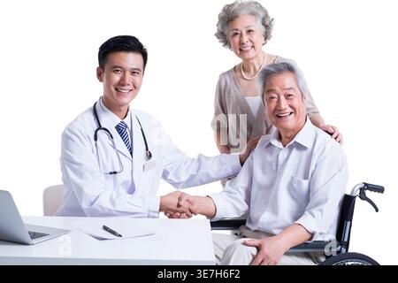 Ein lächelnder chinesischer Arzt schüttelt einem älteren chinesischen Mann die Hand, während er in der Nähe einer älteren chinesischen Frau vor weißem Hintergrund im Studio sitzt Stockfoto