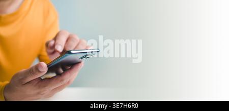Zugeschnittenes Bild eines Mannes mit Smartphone vor weißer Wand Stockfoto