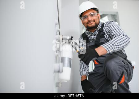 Indischer Klempner mit Uniform und Schutzhelm, der Wasserausrüstung im Badezimmer installiert Stockfoto