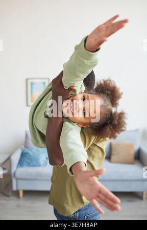 Schwarzer Vater, der seine Tochter trägt und Spaß beim gemeinsamen Spielen im Wohnzimmer zu Hause hat Stockfoto