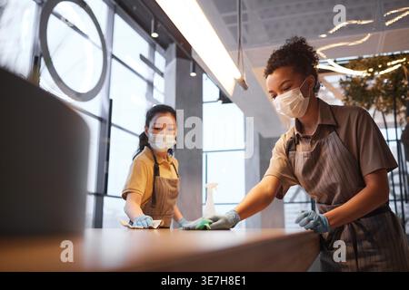Asiatische und gemischte Kellnerinnen mit Gesichtsmasken und Schürzen, die während der Pandemie im Café stehen Stockfoto