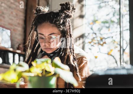 Hispanische Frau mit Dreadlocks, die eine Brille trug und tagsüber am Tisch im Coffee Shop stand Stockfoto