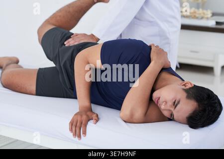 Asiatischer männlicher Patient mit körperlicher Rehabilitation bei männlichem Therapeuten in der Klinik Stockfoto