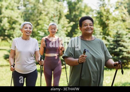 Schwarze Frau mit Trekkingstöcken, die mit Freundinnen im Park an sonnigen Tagen spazieren gehen Stockfoto