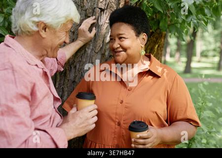 Schwarze Frau mittleren Alters mit einem kaukasischen älteren Mann, der Kaffeetassen hält, während er im Park steht Stockfoto