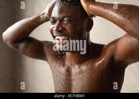Schwarzer Mann, der Shampoo auf die Haare aufträgt, während er im Badezimmer zu Hause duscht Stockfoto