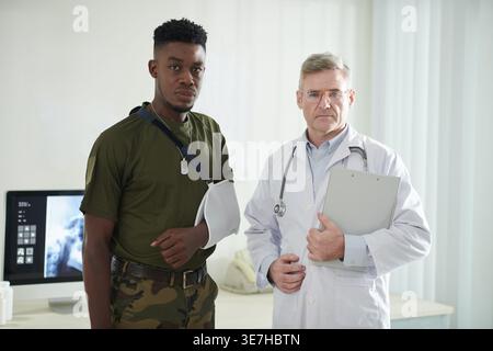 Seriöser Schwarzer Militär und kaukasischer Arzt in Uniform in der Klinik Stockfoto