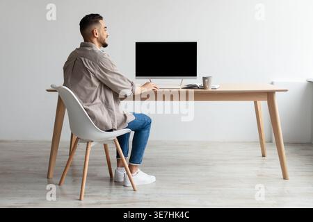 Ein lächelnder Mann aus dem Nahen Osten, der am Computer arbeitet und zu Hause am Tisch sitzt Stockfoto