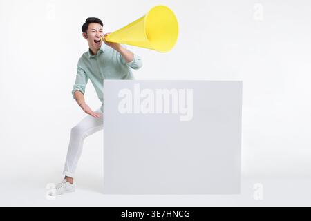 Ein chinesischer Mann, der auf Megaphon schreit und wegschaut, während er hinter dem Whiteboard vor weißem Hintergrund im Studio steht Stockfoto