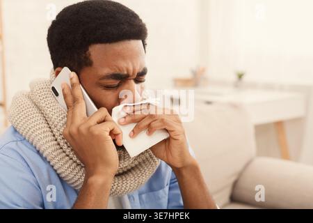 Der kranke Schwarze Mann bläst die Nase auf das Taschentuch, während er zu Hause mit geschlossenen Augen auf dem Sofa sitzt Stockfoto