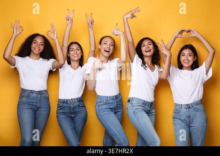 Verschiedene Frauengruppen in Hemden und Jeans mit verschiedenen Handschildern, die im Studio auf gelbem Hintergrund stehen Stockfoto