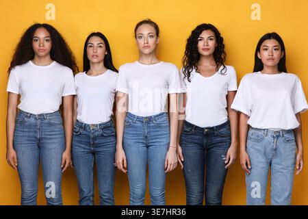 Eine Gruppe von Frauen mit weißen Hemden und Jeans, die im Studio vor gelbem Hintergrund stehen Stockfoto