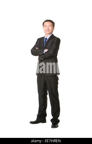 Chinesischer Geschäftsmann mit überkreuzten Armen, der vor weißem Hintergrund im Studio steht Stockfoto