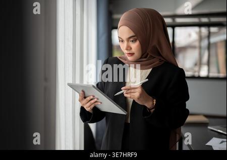 Asiatische Geschäftsfrau im Hijab, die Stifte und Tablets im Büro verwendet Stockfoto