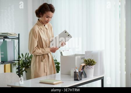 Asiatische Geschäftsfrau, die persönliche Sachen aus der Kiste nimmt und am Schreibtisch im Büro steht Stockfoto