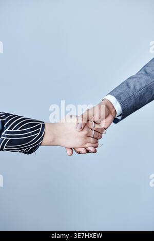 Hände eines schwarzen Geschäftsmannes und einer Frau, die Hände schütteln, die im Büro vor grauem Hintergrund stehen Stockfoto
