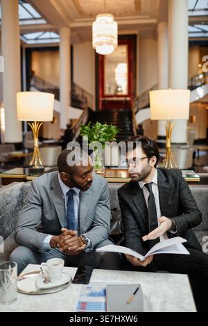 Schwarze und nahöstliche Geschäftsleute diskutieren Arbeit am Tisch in der Hotellobby Stockfoto