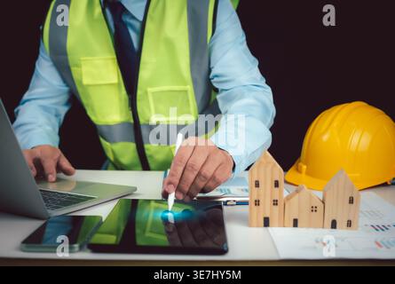Zugeschnittenes Bild eines männlichen Architekten mit Laptop und Eingabestift auf Tablet vor dunklem Hintergrund Stockfoto