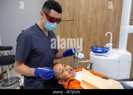 Schwarzer Junge bei zahnärztlicher Behandlung mit kaukasischem Zahnarzt in der Klinik Stockfoto