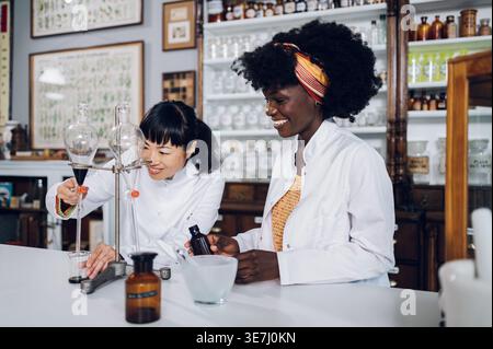 Japanische Chemikerin und schwarze Kollegin, die an einem Experiment mit Separationstrichter und Mörtel in Vintage-Phaar... Stockfoto
