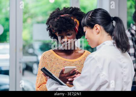 Schwarze Patientin und Kundin spricht mit japanischer Apothekerin über verschreibungspflichtige Medikamente und erhält Kundensupport... Stockfoto