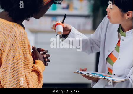 Zugeschnittenes Bild einer schwarzen Patientin und Kundin, die mit einer japanischen Apothekerin spricht, die Salbenspender und Klemmbrett hält... Stockfoto