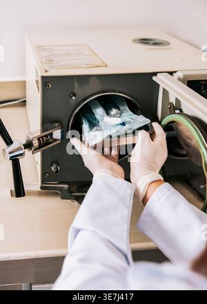 Hispanische Zahnarztin in Latexhandschuhen zur Sterilisation von Werkzeugen mit Autoklaven in der Zahnklinik Stockfoto