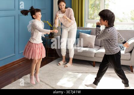 Chinesische Mutter, die ein Video ihrer Kinder macht, die an sonnigen Tagen zu Hause tanzen Stockfoto