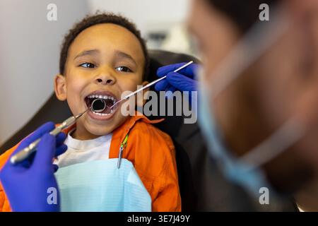 Schwarzer Junge bei Zahnbehandlung mit männlichem Zahnarzt in der Klinik Stockfoto
