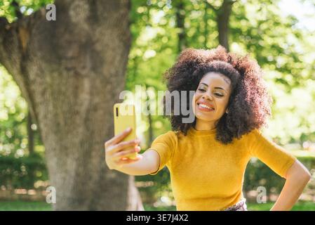 Lächelnde hispanische Frau mit lockigem Haar, die tagsüber im Park steht Stockfoto