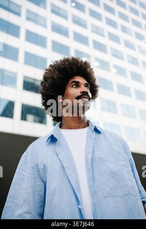 Ernster Schwarzer Mann mit Afro-Frisur und Schnurrbart, der tagsüber in der Nähe des Gebäudes in der Stadt steht Stockfoto