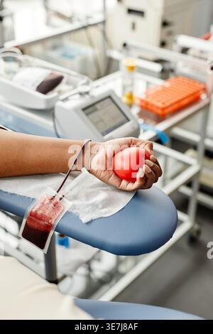 Schwarzer Frauenarm spendet Blut mit rotem Herz-Squeeze-Ball in der Klinik tagsüber Stockfoto