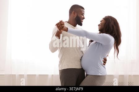Schwarzer Mann tanzt mit schwangeren Frauen im Schlafzimmer zu Hause Stockfoto