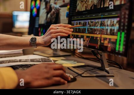 Schwarzer, männlicher Grafiker, der Fotos am Computer bearbeitet, mit einer kaukasischen Kollegin, die auf den großen Bildschirm zeigt und am Tisch im Büro sitzt Stockfoto