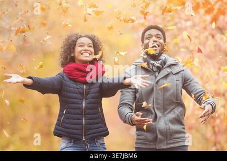 Fröhliches schwarzes Paar, das tagsüber Blätter wirft und Spaß im Herbstpark hat Stockfoto