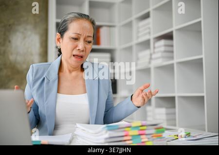 Stressreize ältere asiatische Frau, die sich Dokumente ansieht, die am Tisch im Büro sitzen Stockfoto