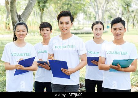 Vietnamesische Freiwillige tragen weiße Hemden mit Bleistiften und Klemmbrettern, die am sonnigen Tag im Park stehen Stockfoto
