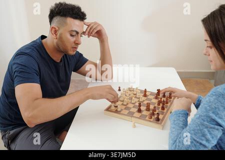 Gemischte Rasse und kaukasisches Paar spielen zu Hause Schach auf dem Tisch Stockfoto