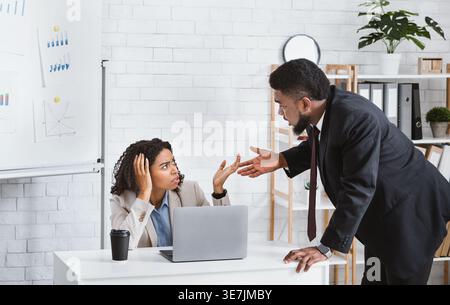 Schwarze männliche und weibliche Angestellte, die sich während der Arbeit im Büro gegenüberstehen Stockfoto
