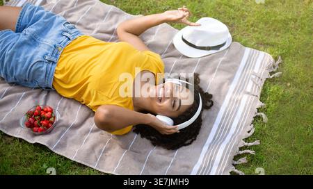 Blick über Black Woman mit Kopfhörern genießt Musik, während Sie auf der Parkdecke liegen Stockfoto