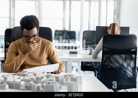 Müder afroamerikanischer Architekt, der Baupläne im Büro überprüft Stockfoto